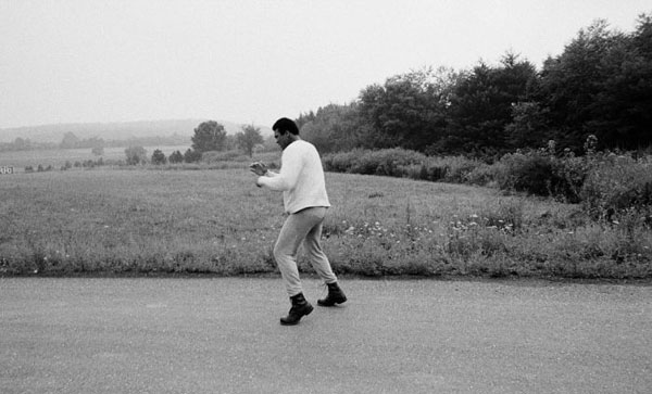 A black and white photo of a man riding a skateboard in a field.