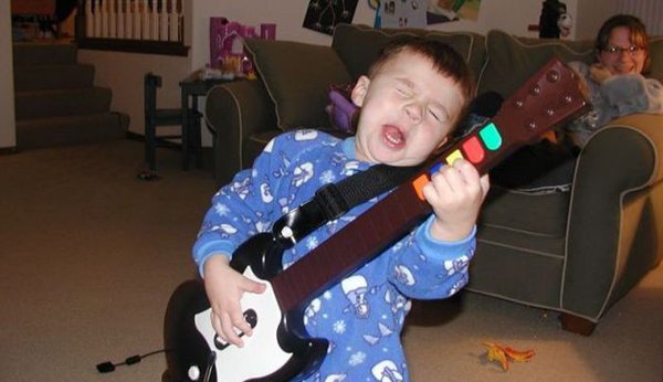 A young boy rockstar performing on guitar in a living room with flair.