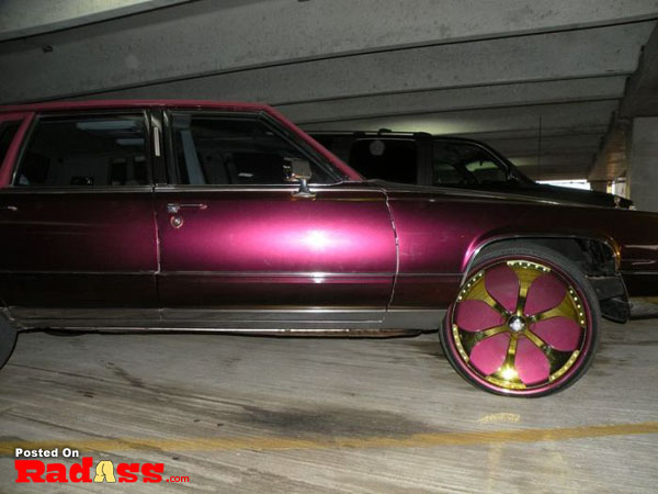 A purple car with gold rims parked in a parking garage, anticipating attention.