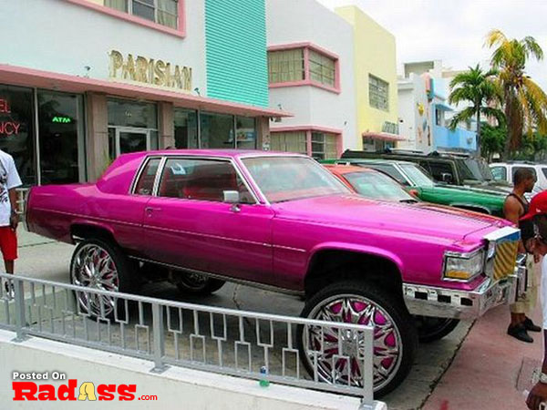 A pink cadillac conspicuous in front of a building.