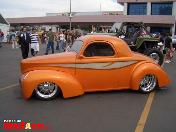 A hot rod car is parked in a parking lot, attracting attention.