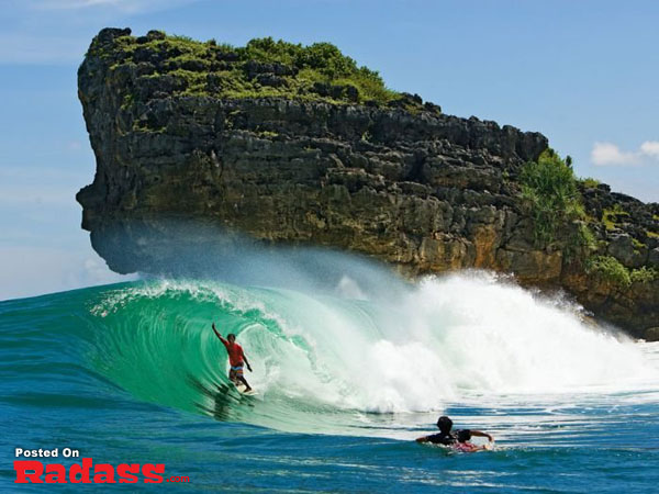 A surfer riding a wave near a rock formation, creating an I'm Going Here moment.