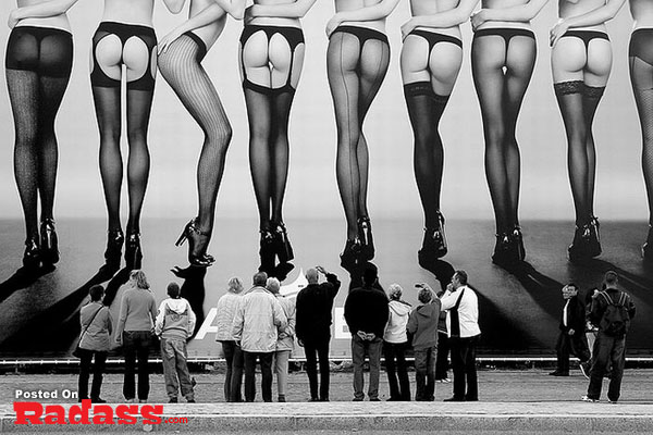 A black and white photo of a group of people standing in front of a poster, capturing curiosity.