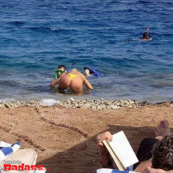 A woman in a bikini is reading a book on the beach.