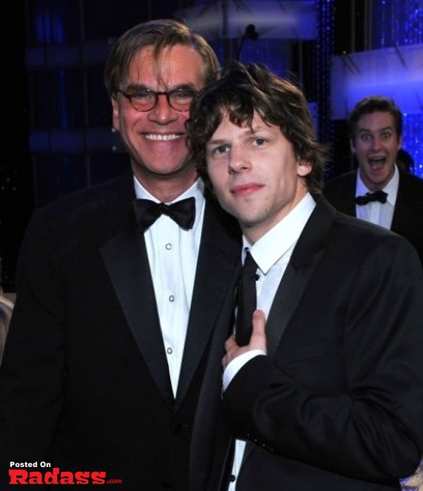 Two men in tuxedos photobombing a celebrity.