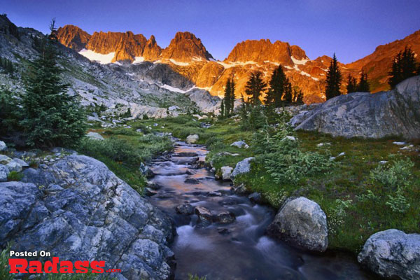 A serene stream cuts through the rugged mountains, providing an idyllic escape from civilization as the sunset paints the sky.