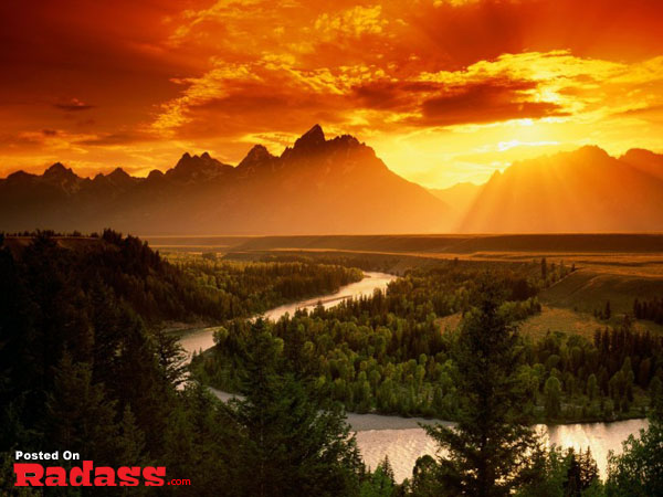 Escape from civilization as the sun sets over a serene river and majestic mountains.