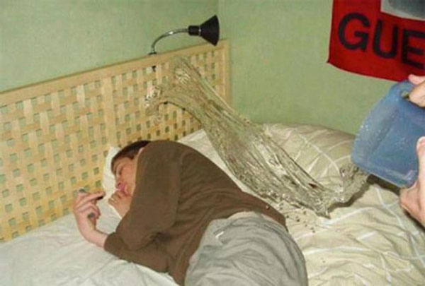 A man lies in bed, holding a bottle of water.