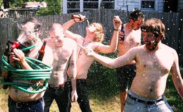 A group of men spraying water on each other in a lively backyard gathering.