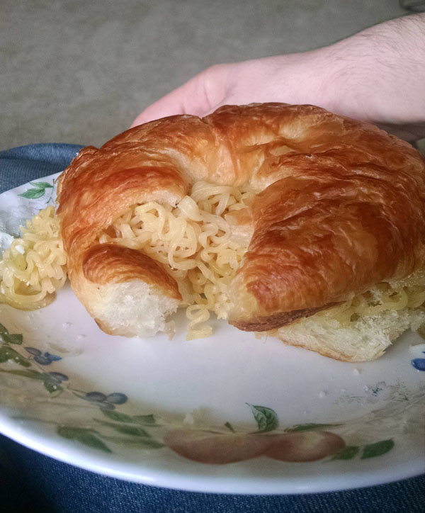 A person is holding a croissant, one of the 16 meals every college student needs to survive, on a plate.