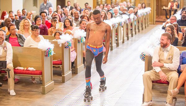 A barechested man on roller skates gracefully glides down the aisle of a church.