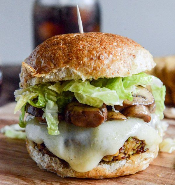 An awesome 2022 burger served on a wooden cutting board with lettuce and mushrooms.