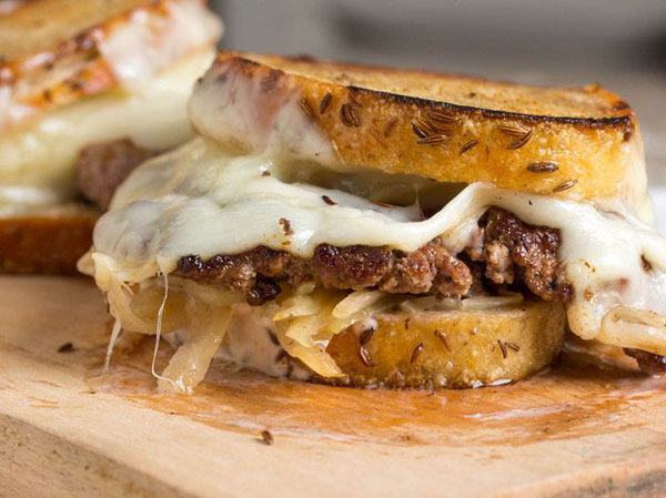 An appetizing grilled sandwich with meat and cheese on a rustic wooden cutting board.