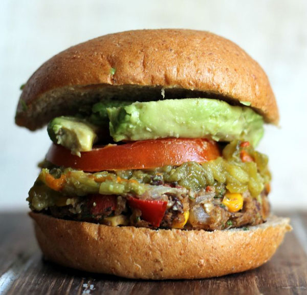 An appetizing avocado and tomato veggie burger displayed on a rustic wooden board.
