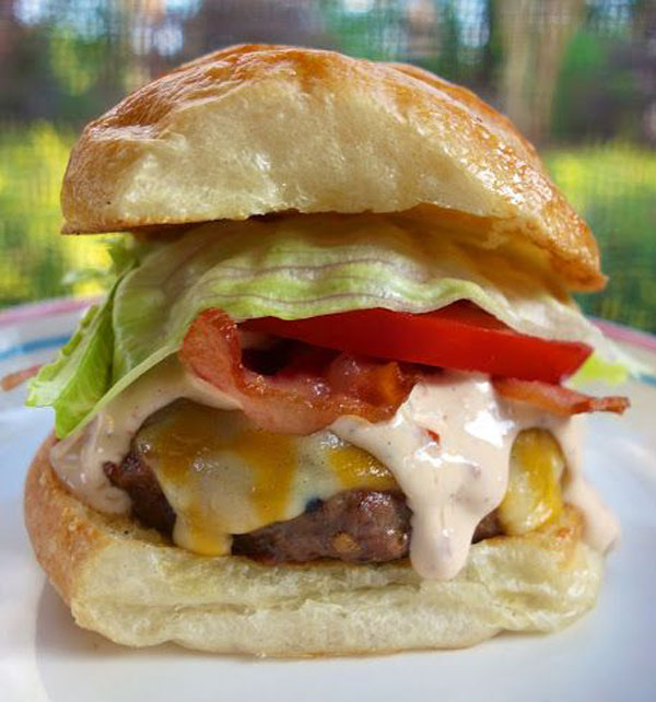 A delicious burger topped with lettuce, tomatoes, and cheese served on a plate.