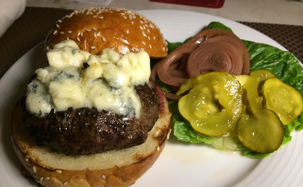 A scrumptious burger topped with blue cheese and pickles, tantalizingly presented on a plate- an awesome burger idea for 2022.
