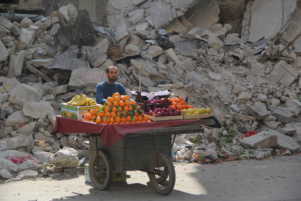 A man selling fruit on a cart in front of rubble, bringing you 40 Cool Pics Just To Make Your Day.