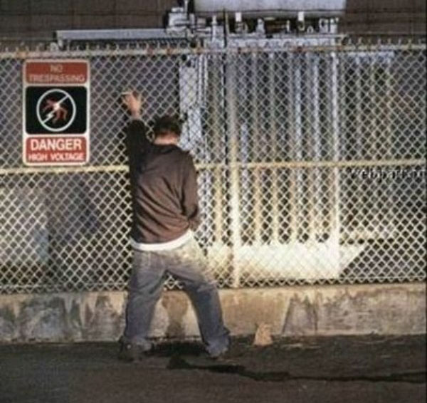 A man drinking excessively with friends leans against a chain link fence.