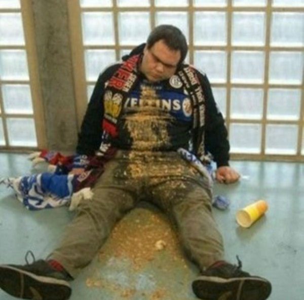 A man, drinking excessively with friends, lays on the floor covered in crumbs.
