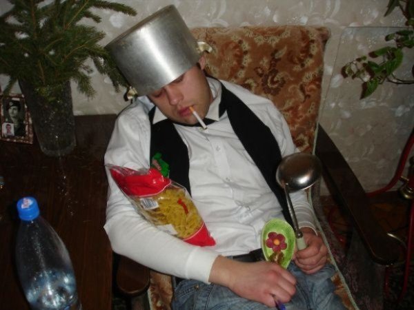 A man, drinking excessively with friends, is sleeping in a chair with a hat on his head.