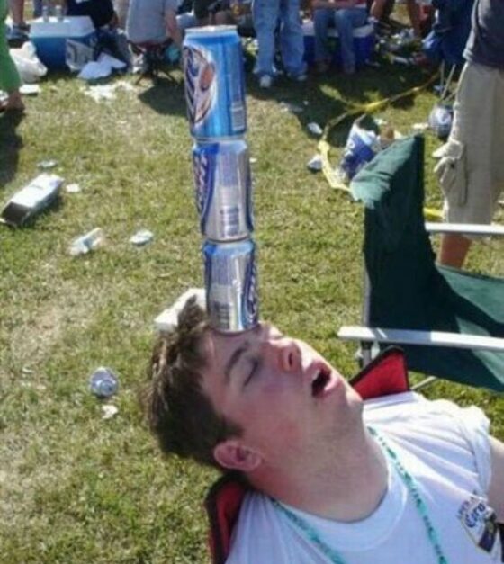 A man drinking excessively with friends is sitting in a lawn chair with beer cans on his head.