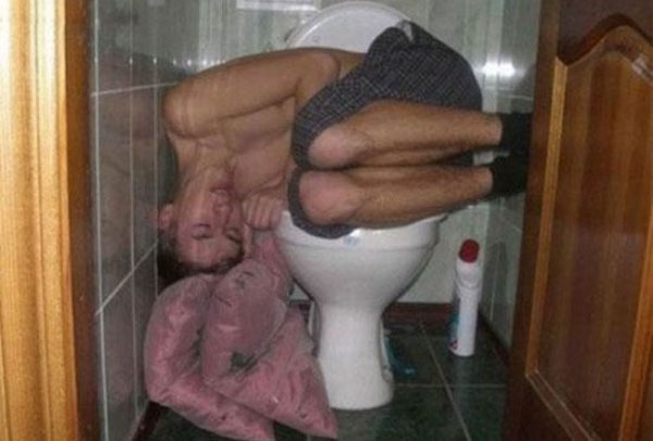 A man drinking excessively with friends in a bathroom.