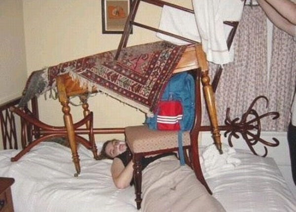 A woman drinking excessively on a bed with a chair on top of it.