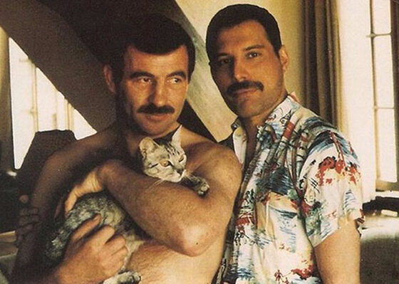 Two men holding a cat in a living room - Freddie Mercury and Jim Hutton.