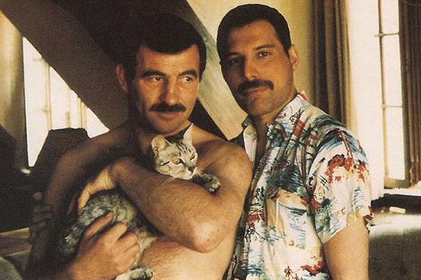 Two men holding a cat in a living room - Freddie Mercury and Jim Hutton.