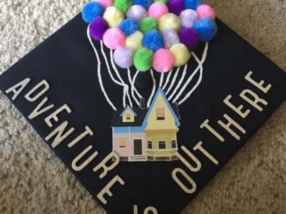 A graduation cap adorned with pom poms that humorously showcases the message "adventure is out there.
