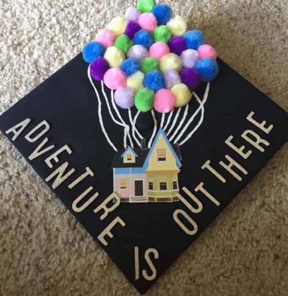 A graduation cap adorned with pom poms that humorously showcases the message "adventure is out there.