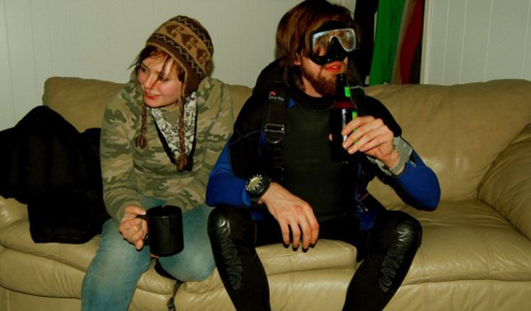 A man and woman sitting on a couch with a beer and a bottle.