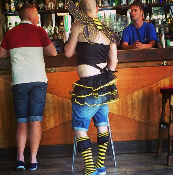 A man dressed as a bee standing in front of a hipster bar.