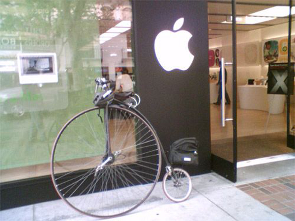 A hipster bicycle parked outside an apple store.