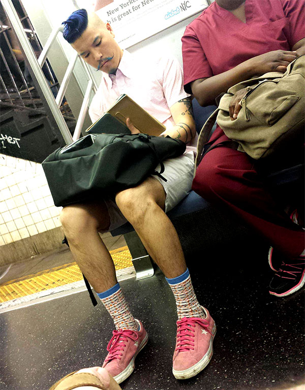 A man sitting on a train while hipsters have gone too far.
