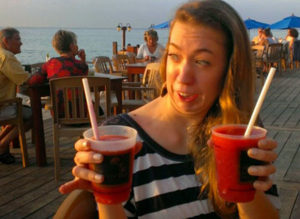 A woman holding two drinks on a wooden deck.
