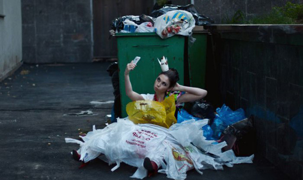 A woman sitting on the ground next to a trash can, contemplating 