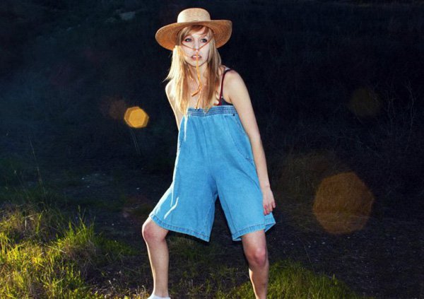 A woman in denim overalls standing in a field.