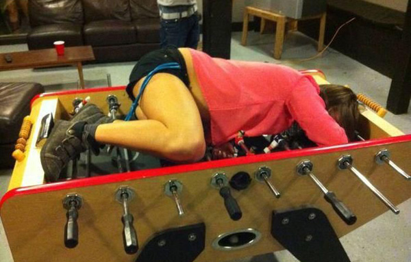 A woman lounging on the foosball table, surrounded by laughter and friendly banter.