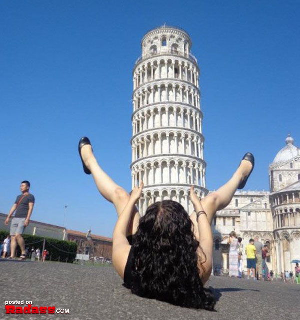 A woman happily laying on the ground in front of the leaning tower of Pisa.