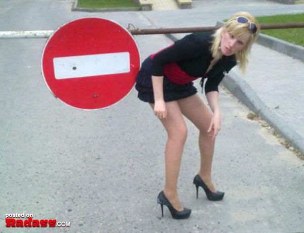 A woman in high heels leaning against a street sign, expressing 