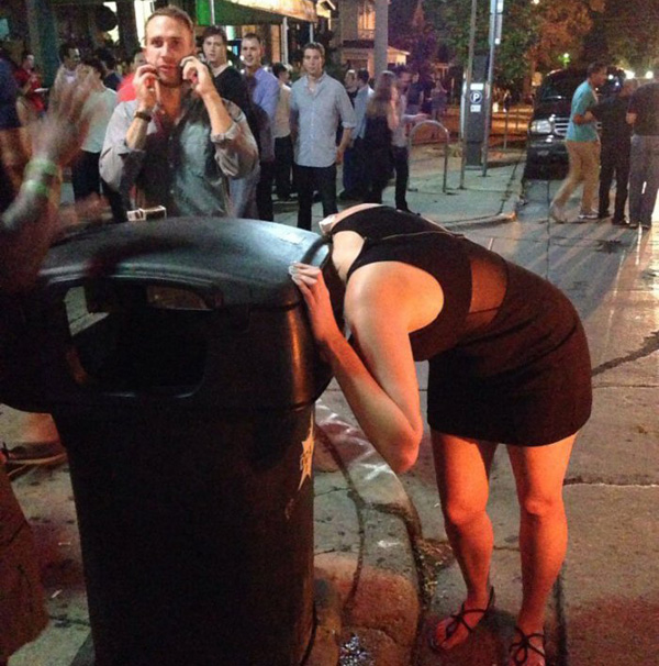 A woman in a black dress leaning over a trash can, contemplating the phrase 