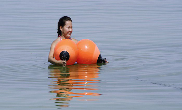 A woman is floating in the water with an orange float, contemplating 