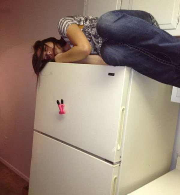 A woman playfully lounging on top of a refrigerator.