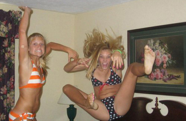 Two girls in bikinis playfully jumping on a bed.