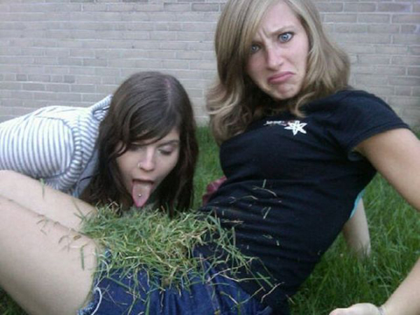 Two girls laying on the grass with their tongues out, playfully sticking them out as if to say 