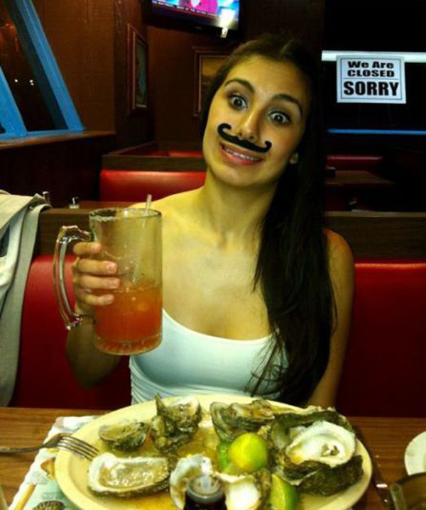 A woman with a mustache holding a plate of oysters, making it hard to resist saying 