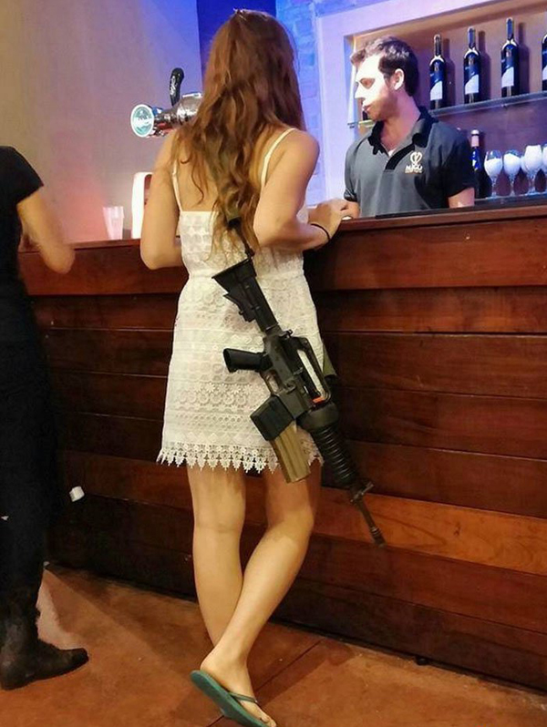 A woman in a white dress with a rifle standing next to a bar, showcasing her bold and adventurous spirit that says 