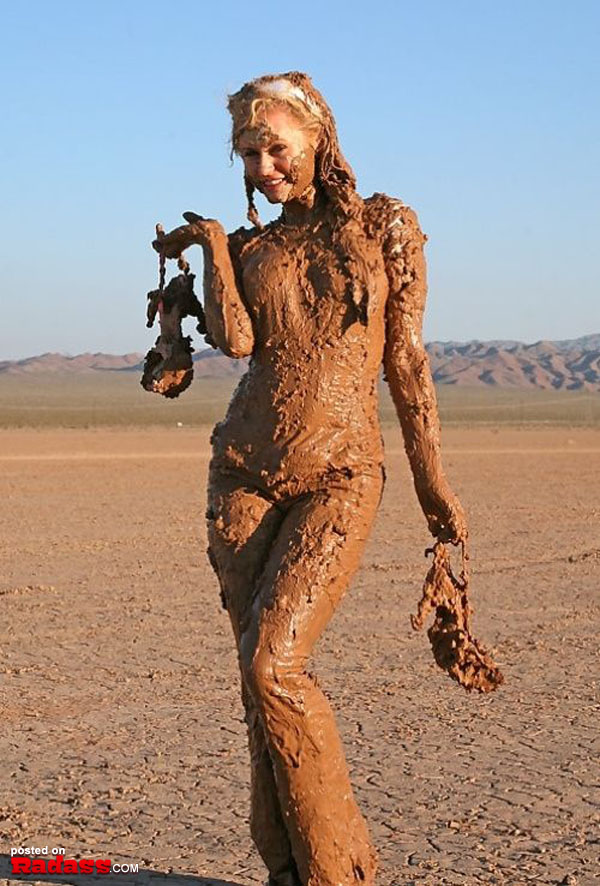 A woman standing in the desert covered in mud.