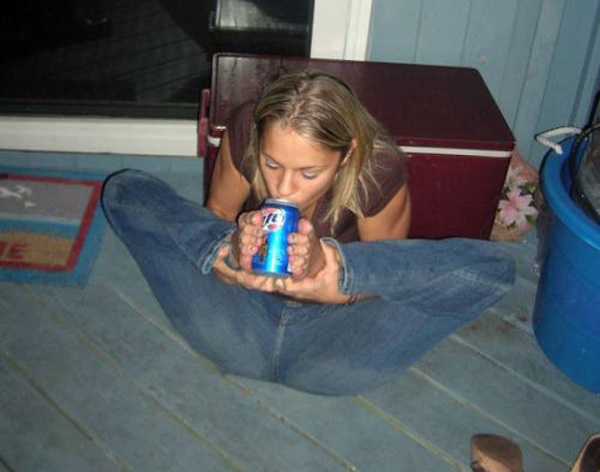 A woman sitting on the floor drinking a beer while playfully saying 
